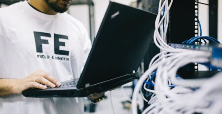 serious ethnic field engineer examining hardware and working on laptop